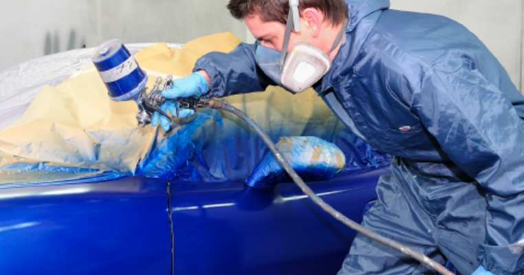 pintando un auto azul mientras se usa equipo de protección personal