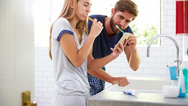 man and woman brushing their teeth